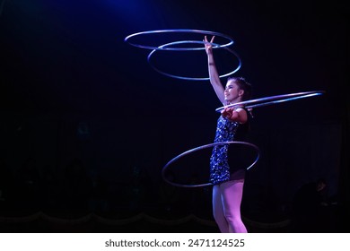 Young slim attractive circus gymnast woman performing live show with hula hoops on red arena with blue backlight, audience is excited - Powered by Shutterstock