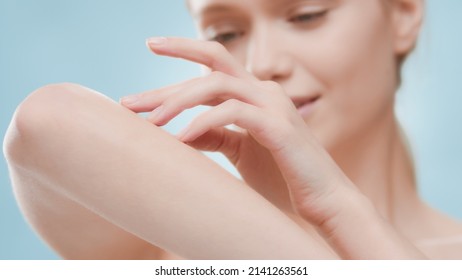 Young slim attractive European blond woman touches her forearm smooth skin against blue background | Body skin care and unwanted hair removal commercial concept - Shutterstock ID 2141263561
