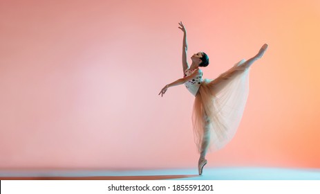 Young slim ballerina in a light long dress is dancing on a colored background with backlight - Shutterstock ID 1855591201