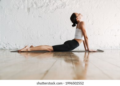 Young slim brunette fitness woman stretching on a sports mat in the studio side - Shutterstock ID 1996502552