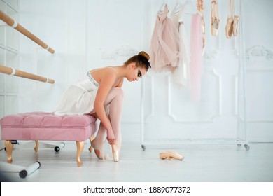 Young Slim Dancer Puts On Pointe Shoes, Sitting On A Ottoman - Bench. Photo In The Dance Hall.