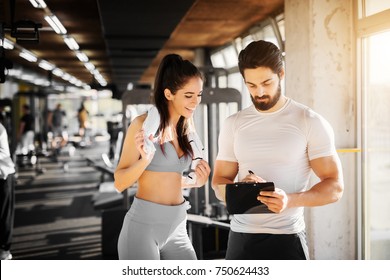 Young slim fitness girl standing with a towel near handsome trainer while showing her schedule for next week in the gym. - Powered by Shutterstock