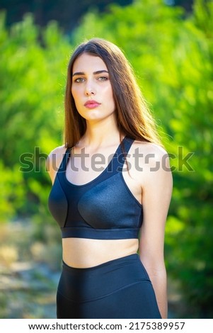 Young slim girl in a black sports leotard against the background of a green forest