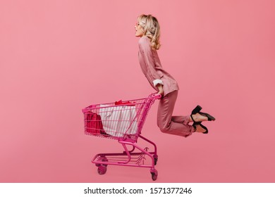 Young slim girl in pink suit riding cart from store