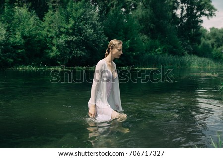 young slim girl posing in cold water. a warm summer day in Park street. hair in a bun, clean skin. clothing style: transparent blouse. Wallpaper for desktop