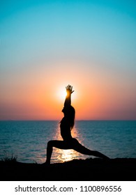 Young Slim Girl Practicing Yoga On Mountain Against Ocean Or Sea At Sunrise Time. Silhouette Of Woman In Rays Of Awesome Sunset.