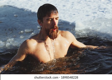 young, slim, handsome, sporty man with a red beard and long hair, naked, in black shorts, diving into ice-cold water in winter, against the backdrop Ukraine, Shostka