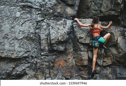 young slim muscular woman rockclimber climbing on tough sport route, searching, reaching and gripping hold. climber makes a hard move. outdoors rock climbing and active lifestyle concept