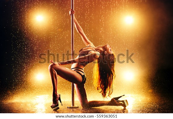 Young slim sexy\
brunette woman pole dancing in club interior with light, smoke and\
rain. Vibrant warm\
colors.