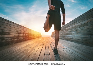 Young slim sporty man warming and stretching legs before run outdoors at sunset or sunrise. Athletic man in black sportswear doing fitness stretching exercises. Sport and healthy lifestyle.