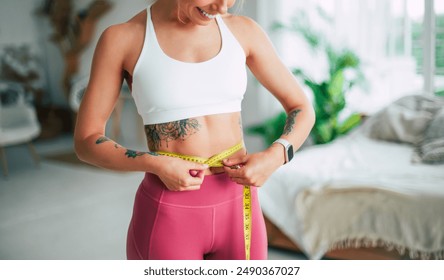 Young slim strong sporty athletic fitness trainer instructor woman in sportswear holds measure tape on waist training do exercises at home gym. Workout, sport, motivation. Female losing weight - Powered by Shutterstock