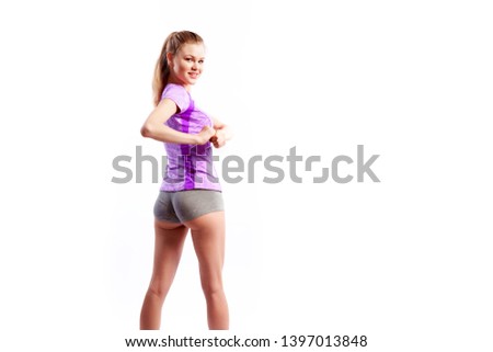 A young  slim woman athlete  in a sporty pink top and shorts makes turns a side and smilling on a  white isolated background in studio, back view. Portrait of a beautiful sportswoman