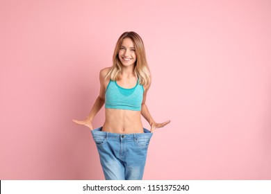 Young slim woman in old big jeans showing her diet results on color background