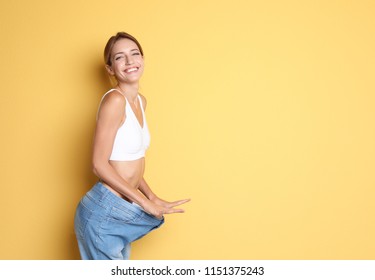 Young slim woman in old big jeans showing her diet results on color background - Shutterstock ID 1151375243