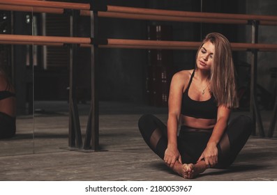 Young slim woman in sports uniform works out in evening in an old gym, doing stretching exercises at mirror. Female doing fitness training. Concept of healthy lifestyle, sport and exercise in gym