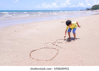 Young Small Active Child Writing And Drawing On The Sand Beach At The Sea Shore With Little Wood Stick During Beautiful Sunny Day In Summer Time