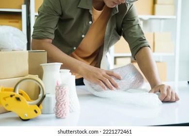 Young Small Business Entrepreneur Man, Online Store Owner With Shelves Of Boxes In The Background Packing Product In Mailing Box At Workplace For Shipping To Customer. Selling Product Online.