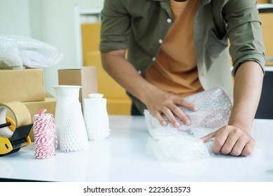 Young Small Business Entrepreneur Man, Online Store Owner With Shelves Of Boxes In The Background Packing Product In Mailing Box At Workplace For Shipping To Customer. Selling Product Online.