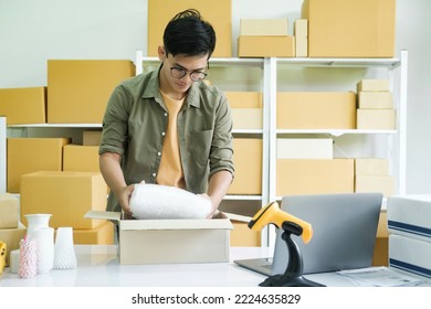 Young Small Business Entrepreneur Man, Online Store Owner With Shelves Of Boxes In The Background Packing Product In Mailing Box At Workplace For Shipping To Customer. Selling Product Online.