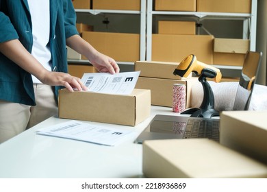 Young Small Business Entrepreneur Woman, Online Store Onwer With Shelves Of Cardboard Boxes In The Background Packing Product In Mailing Box, Labeling Delivery Package For Shipping To Customer.