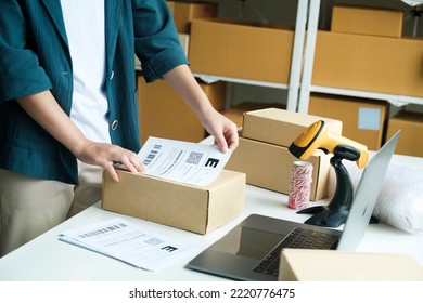 Young Small Business Entrepreneur Woman, Online Store Onwer With Shelves Of Cardboard Boxes In The Background Packing Product In Mailing Box, Labeling Delivery Package For Shipping To Customer.