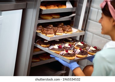 A young small business female owner fills the closet with delicious handmade donuts in a pleasant atmosphere in a candy workshop. Pastry, dessert, sweet, making