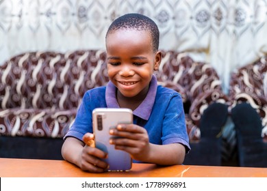 Young Smart Black African Boy Browsing The Internet Using Digital Phone Smiling Siting Down. Technology Concept