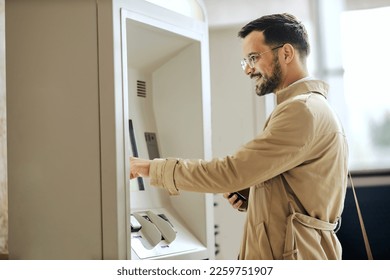 A young smart casual man is using ATM.