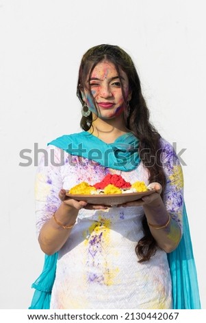 Young smart indian girl with plate full of color powder and face coloured with gulal for festival of colours Holi, a popular hindu festival celebrated across india, isolated over white background