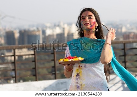 Young smart indian girl with plate full of color powder and face coloured with gulal for festival of colours Holi, a popular hindu festival celebrated across india