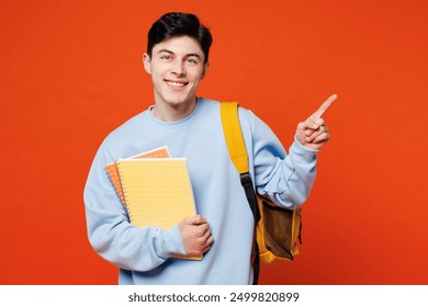 Young smart man student he wear blue casual clothes backpack bag hold books point index finger aside on empty free area isolated on plain red orange background. High school university college concept - Powered by Shutterstock