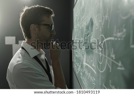 Young smart mathematician drawing math formulas on the chalkboard and thinking: he is solving problems and discovering new theories