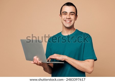 Young smart IT middle eastern man wear blue t-shirt casual clothes hold use work on laptop pc computer look camera isolated on plain pastel light beige background studio portrait. Lifestyle concept