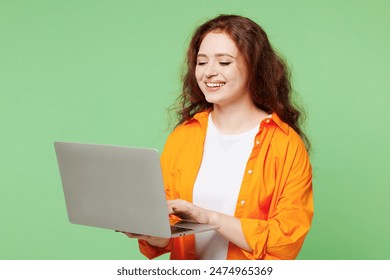 Young smart smiling student ginger IT woman she wear orange shirt white t-shirt casual clothes hold use work on laptop pc computer isolated on plain pastel light green background. Lifestyle concept - Powered by Shutterstock