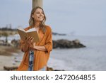 Young smart student calm happy woman she wearing orange shirt casual clothes reading book novel study look aside walking on sea ocean sand shore beach outdoor seaside in summer day. Lifestyle concept