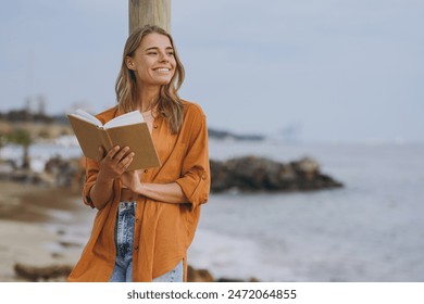 Young smart student calm happy woman she wearing orange shirt casual clothes reading book novel study look aside walking on sea ocean sand shore beach outdoor seaside in summer day. Lifestyle concept - Powered by Shutterstock