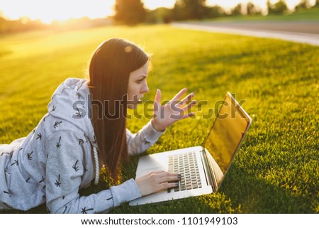 Young smart student female in casual clothes. Woman lying on grass ground, working on laptop pc computer in city park on green grass sunshine lawn outdoors. Mobile Office. Freelance business concept