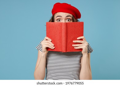 Young smart student woman 20s with short hairdo wearing french beret red hat striped t-shirt hiding cover face mouth with diary read book novel isolated on pastel blue color background studio portrait