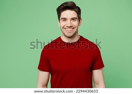 Young smiilng happy fun cheerful satisfied brunet caucasian man he wears red t-shirt casual clothes looking camera isolated on plain pastel light green background studio portrait. Lifestyle concept