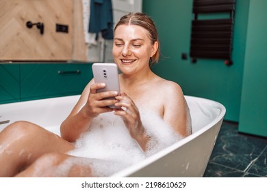 Young smile woman taking a bath and talking on phone, lying in bathtub with foam at home. - Powered by Shutterstock