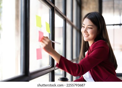 Young smiley attractive, businesswoman using sticky notes in glass wall to writing strategy business plan to development grow to success - Shutterstock ID 2255793687