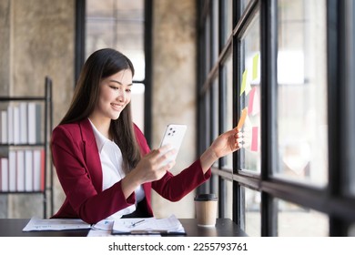 Young smiley attractive, businesswoman using sticky notes in glass wall to writing strategy business plan to development grow to success - Shutterstock ID 2255793761
