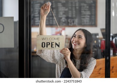 Young smiley female entrepreneur holding open sign board hanging on window glass of cafe. - Powered by Shutterstock