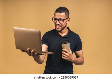 Young Smiling African American Black Man Standing And Using Laptop Computer Isolated Over Beige Background. Drinking Coffee.