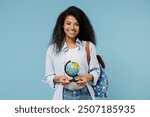 Young smiling african american girl teen geography student wear denim clothes backpack hold in hands Earth world globe isolated on blue background Education in high school university college concept