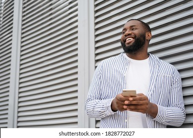 Young smiling African American man using mobile application for online shopping on black Friday. Portrait of handsome businessman holding cellphone, chatting, communication, working online