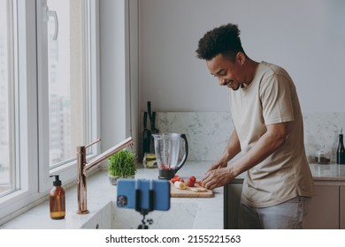 Young Smiling African American Man In Casual Clothes Prepare Sweet Breakfast Cut Fruit Watch Series On Mobile Cell Phone Cooking Food In Indoor Kitchen At Home Alone Healthy Diet Lifestyle Concept.