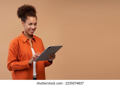 Young smiling African American woman using digital tablet isolated on beige background, copy space. Happy successful female shopping online. Technology concept 