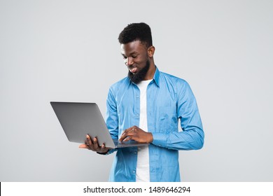 Young smiling african man standing and using laptop computer isolated over gray background