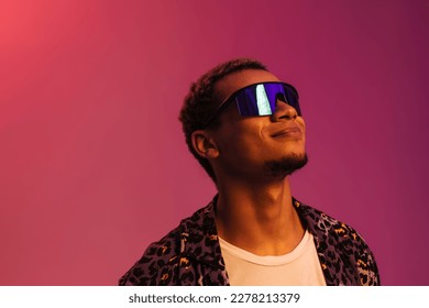 Young smiling african man wearing sunglasses   leopard shirt posing isolated over pink neon background